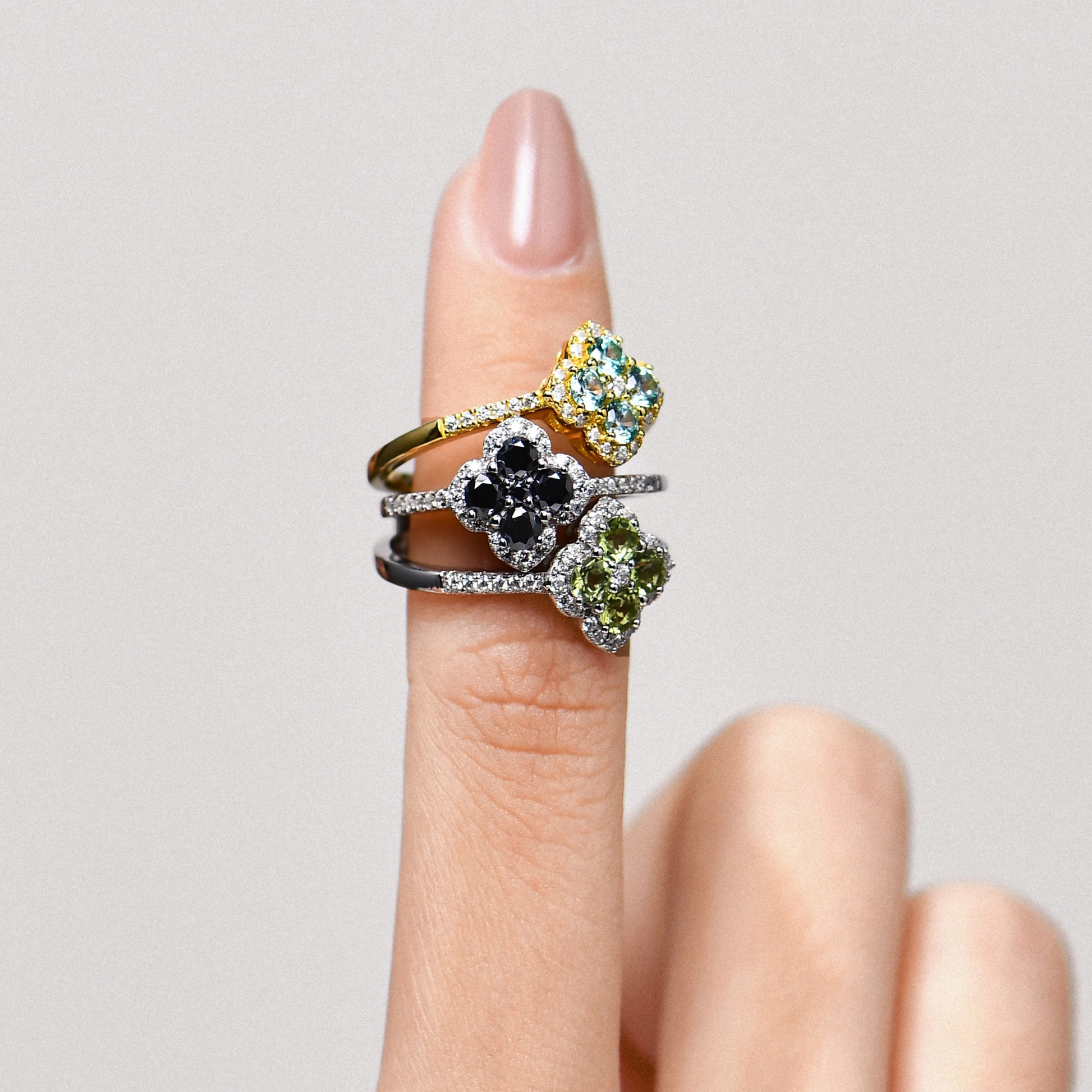 Three clover rings with moissanite gemstones on a finger against a neutral background