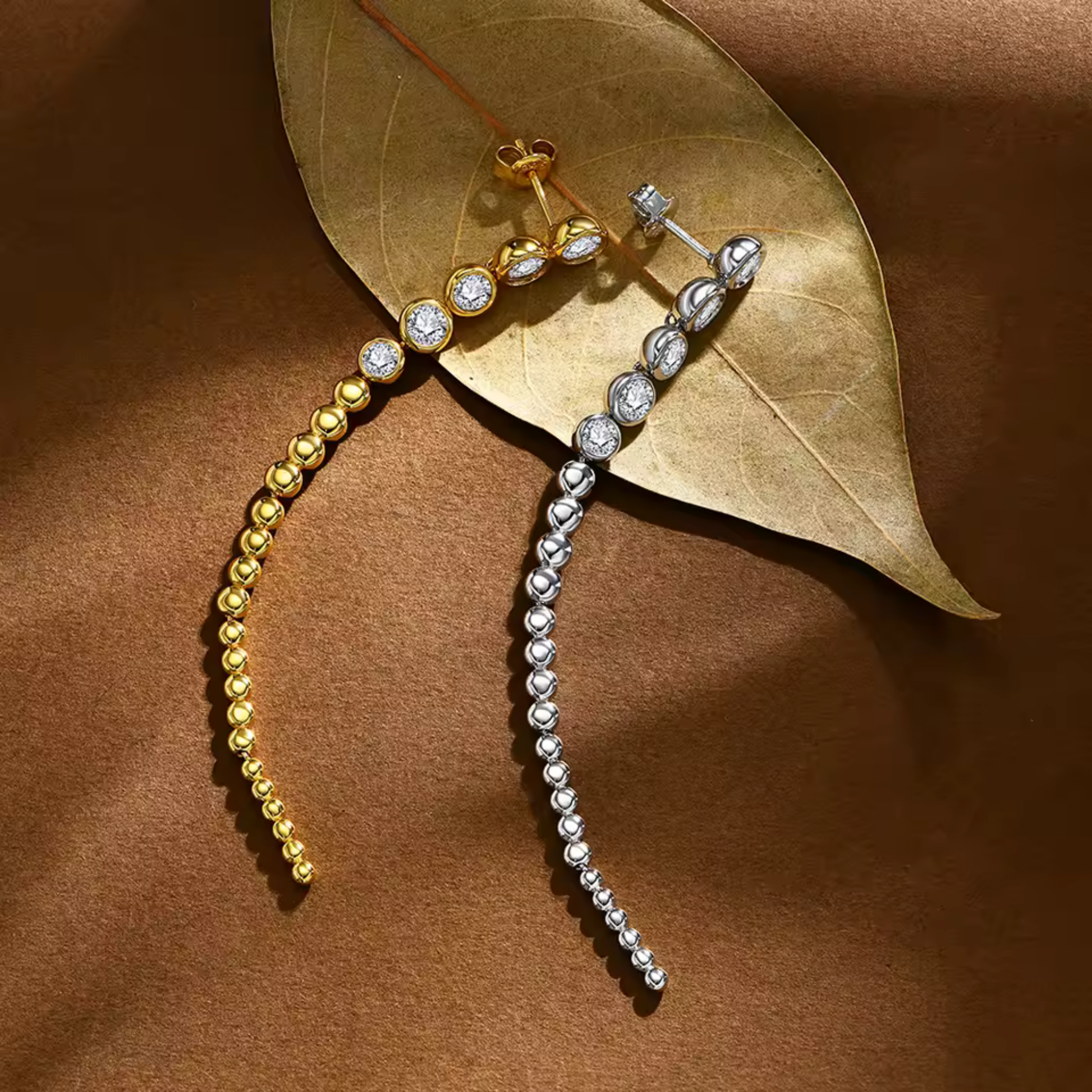 Gold and silver moissanite beaded earrings on a brown leaf