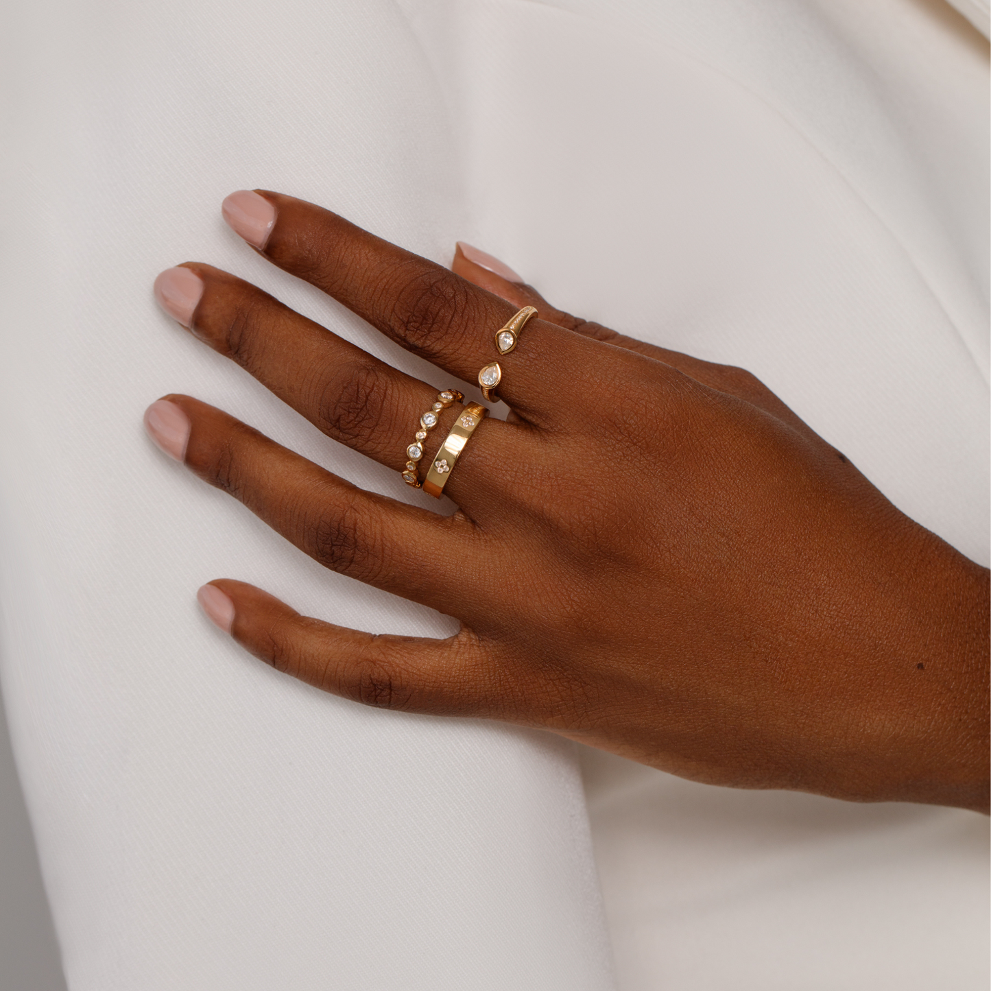 Hand wearing stacked gold rings adorned with moissanite stones on a neutral background