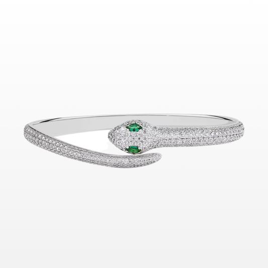 A silver snake shaped wrap-around bracelet with green gemstones for the snake's eyes and white moissanite stone embellishments around its body.